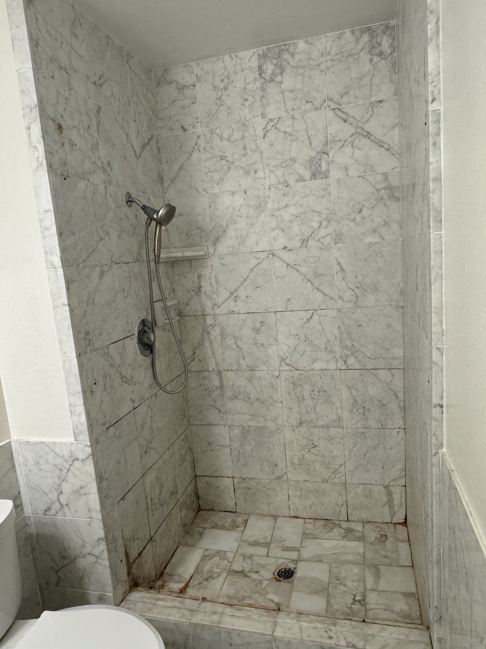 Before refinishing in Palo Alto, CA &mdash; corner shower with grey marble-look tile and mildew-stained grout lines